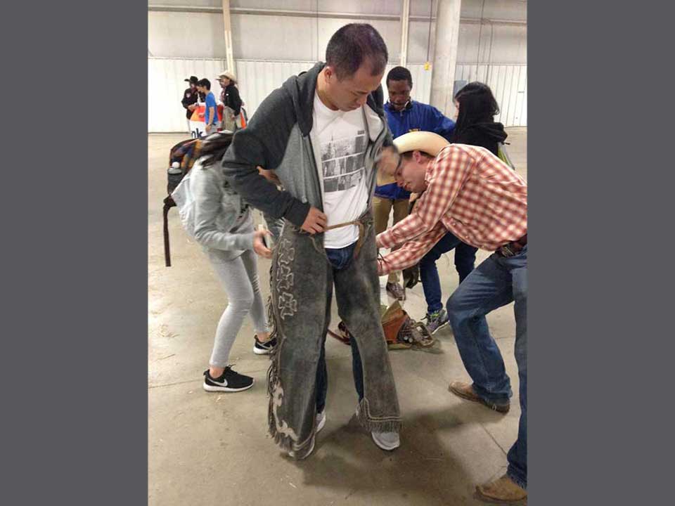 International student tries on chaps at the UNL Rodeo